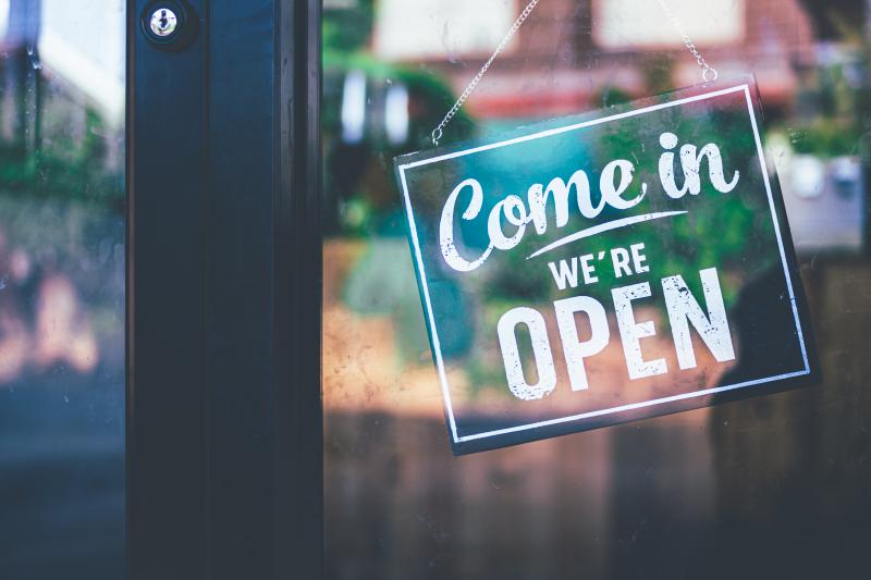 Isang berdeng karatula ang nakasabit sa isang pintong salamin na may nakasulat na "Come in, we're open"